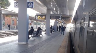 Stazione ferroviaria, banchina, binario, persone in attesa.